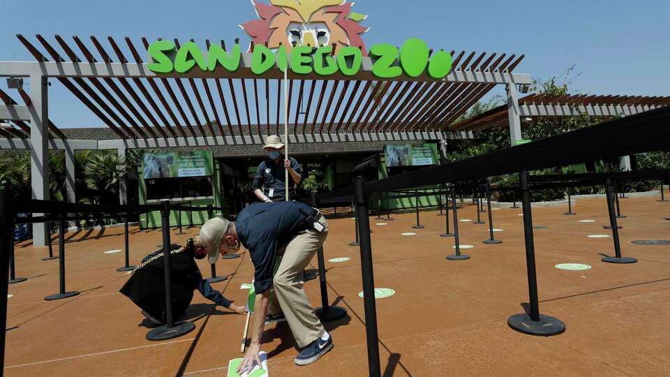 Devon Prince, front, puts down a sticker to guide visitors at the San Diego Zoo once it reopens, as Emmanuel Lopez, behind and Ariel Hayes look on, Thursday, June 11, 2020, in San Diego. California's tourism industry is gearing back up with the state giving counties the green light to allow hotels, zoos, aquariums, wine tasting rooms and museums to reopen Friday. (AP Photo/Gregory Bull)