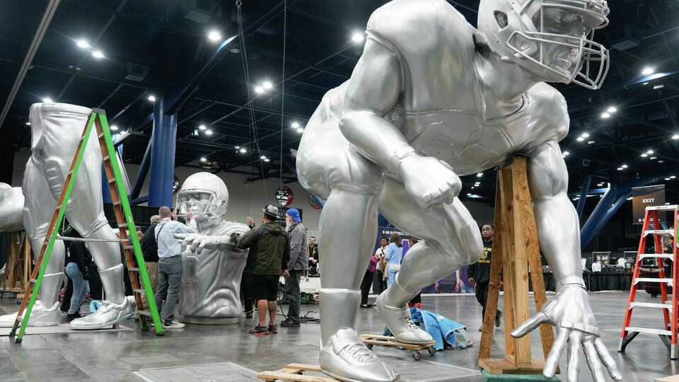 Workers move large statues of football players into place as setup continues at Playoff Fan Central at the George R. Brown Convention Center, Thursday, Jan. 4, 2024, in Houston. The three-day, 300,000 square-foot interactive experience features games, youth sports clinics, pep rallies and exhibits celebrating college football.