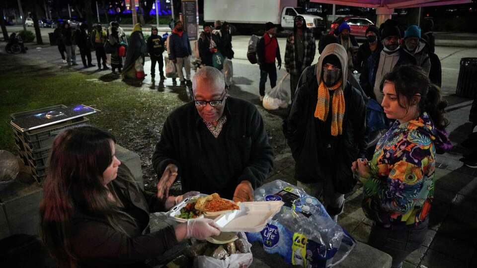 Food Not Bombs volunteer Eric Harris, center, takes a meal tray from fellow volunteer Britt Villalobos as they feed homeless people during a regular meal distribution Wednesday, Jan. 3, 2024, in front of Houston Public Library's Julia Ideson Building in Houston. Harris said he used to come to the distribution and eat a few years ago, but that his circumstances had improved. He said he now brings donations and food and volunteers his time.