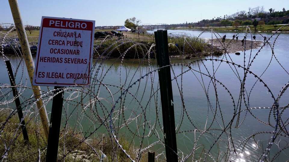 Migrants cross the Rio Grande into the U.S. from Mexico behind Concertina wire and a sign warning that it's dangerous and illegal to cross, Wednesday, Jan. 3, 2024, in Eagle Pass, Texas. According to U.S. officials, a Mexican enforcement surge has contributed to a sharp drop in illegal entries to the U.S. in recent weeks.