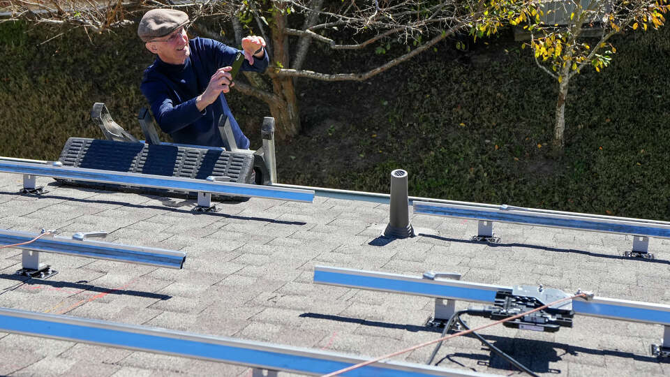 Mickey Lee stands on a ladder taking photos as workers from True Texas Solar install a solar power system, funded through a loan from Capital Good Fund, on his home on Monday, Dec. 11, 2023 in Conroe. Capital Good Fund is providing loans to Houstonians to make rooftop solar more accessible.