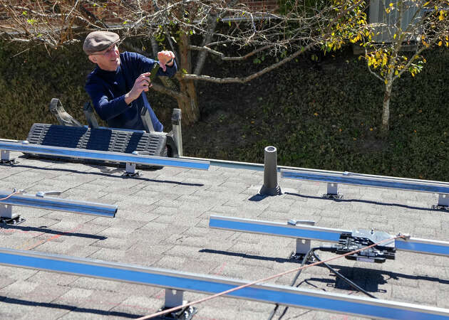 Mickey Lee stands on a ladder taking photos as workers from True Texas Solar install a solar power system, funded through a loan from Capital Good Fund, on his home on Monday, Dec. 11, 2023 in Conroe. Capital Good Fund is providing loans to Houstonians to make rooftop solar more accessible.