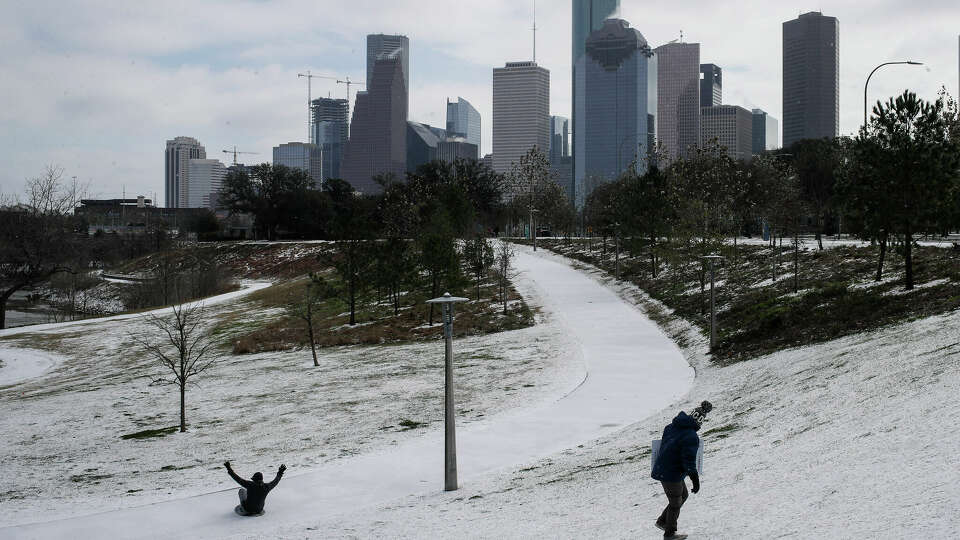 Chris Martinez, right, looks back at a man sliding down a snow-covered hill on Feb. 15, 2021, at Buffalo Bayou Park in Houston. Next week, Texas will experience its coldest temperatures so far this winter, but Houston likely won't see any snow or ice this time.