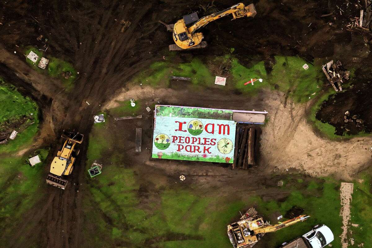 An overhead image shows three construction vehicles removing debris from People's Park in Berkeley, surrounding a structure with a rooftop mural that reads, "I am Peoples Park."