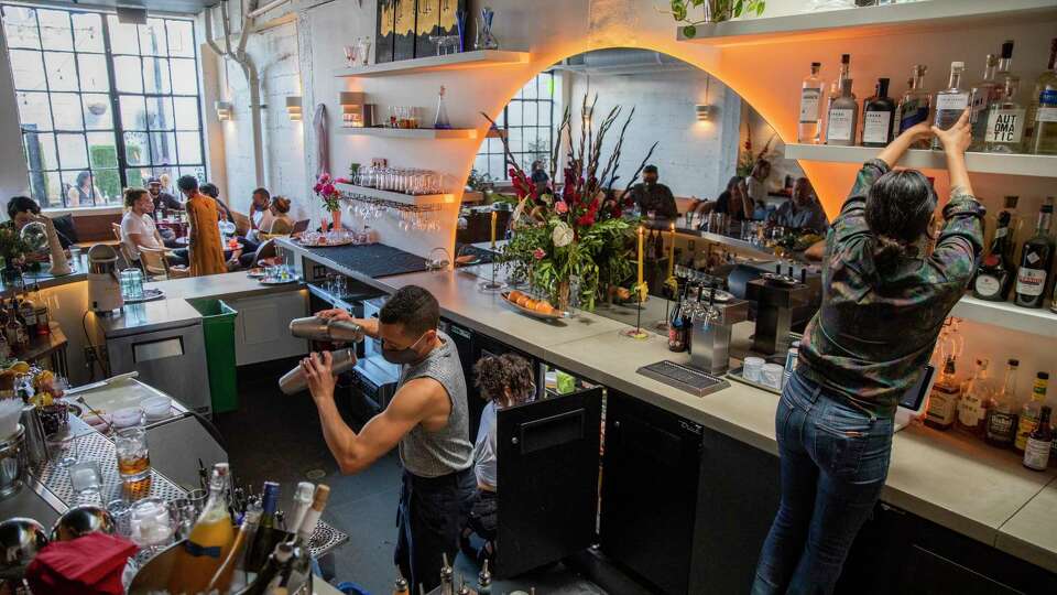 Julian Arreola (left) on the cocktail shakers and Bree Flores (right) on the steps to grab a bottle of alcohol to make drinks for customers at Friends and Family, Saturday, June 12, 2021, in Oakland, Calif. The bar is located at 468 25th St.