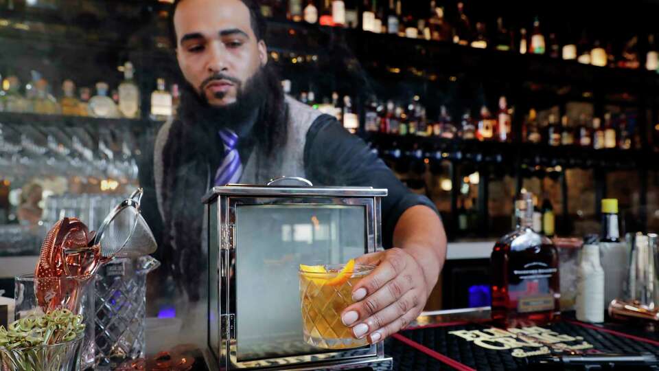 Bartender Zarion Clements removes a ÒSmoking Gun Old FashionedÓ bourbon cocktail from the smoke box at the bar of new Federal American Grill Friday, Mar. 8, 2024 in downtown Houston.