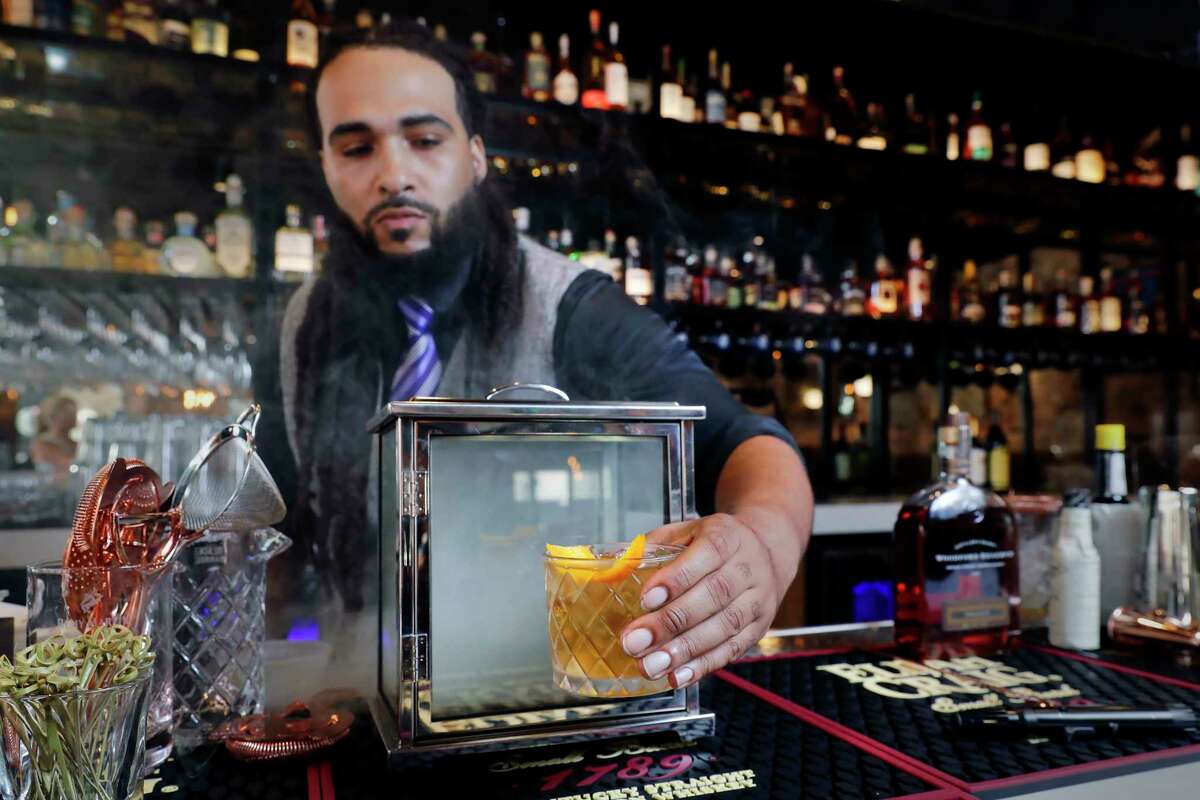 Bartender Zarion Clements removes a 'Smoking Gun Old Fashioned' bourbon cocktail from the smoke box at the bar of new Federal American Grill Friday, Mar. 8, 2024 in downtown Houston.