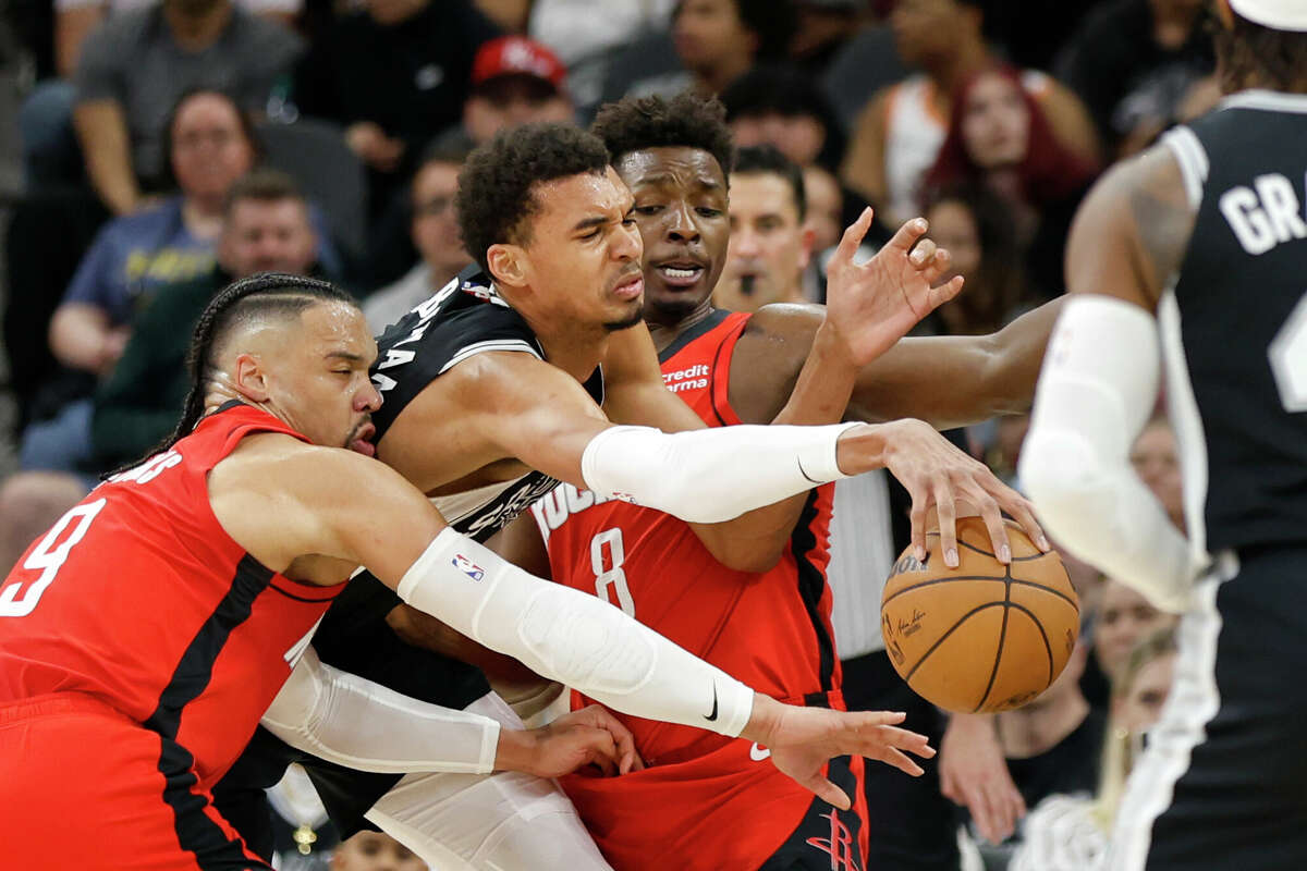 Victor Wembanyama #1 of the San Antonio Spurs scrambles for a lose ball with Dillon Brooks #9 of the Houston Rockets and Jae'Sean Tate #8 in the first half at Frost Bank Center on March 12, 2024 in San Antonio, Texas.