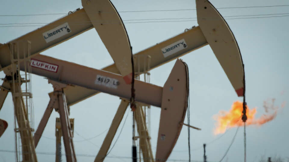 Pumpjacks are obscured by heat as they operate and a flare burns Thursday, July 7, 2022, in Midland.