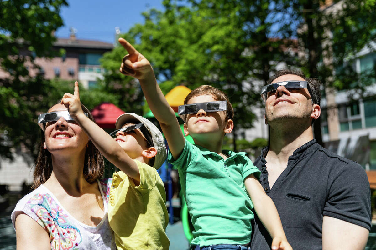 Family looking at solar eclipse in the city street in a public park