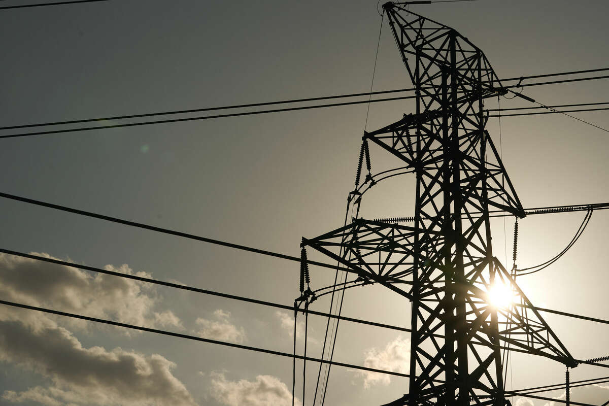 The sun shines through electrical pylons and power lines.