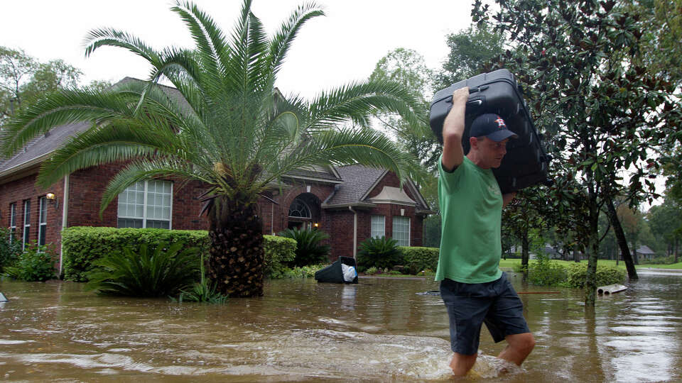 Mike Bartlow carries items out of his house through flood water as his family evacuates their home in River Plantation, Monday, Aug. 28, 2017, in Conroe.