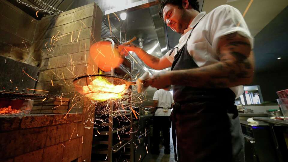 Sparks fly as Chef Max Lappe fans wood coals to raise the heat before using them to grill oysters at Baso, a new restaurant in The Heights Friday, May 3, 2024 in Houston.