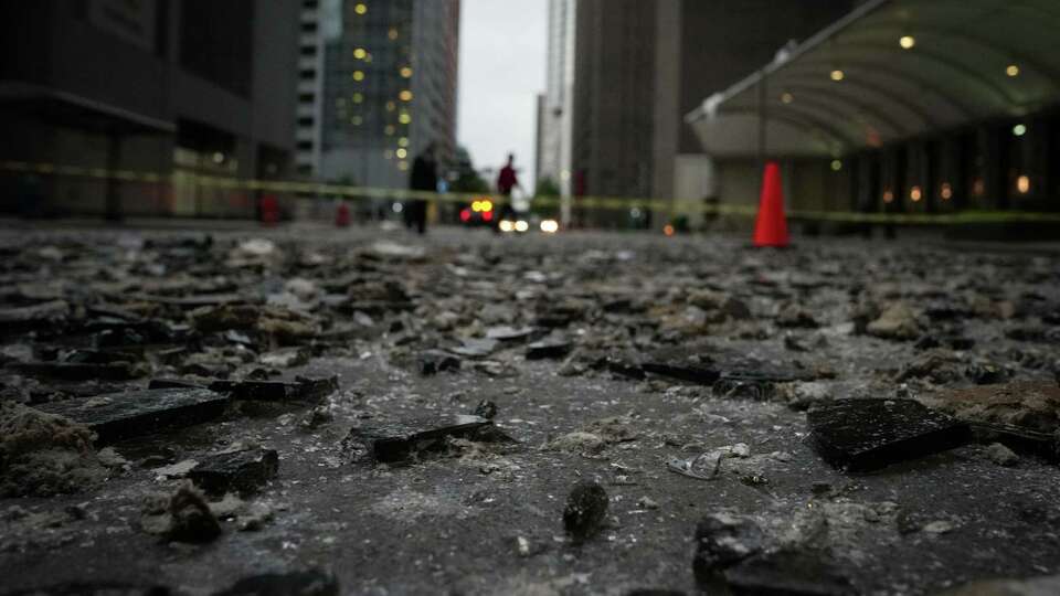 People walk over broken glass to cross Louisiana Street on Friday, May 17, 2024, in downtown Houston.