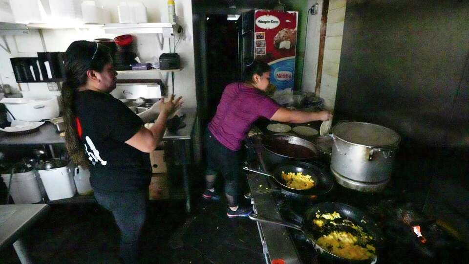 Janet Melgar, left, and Veronica Caal make to go orders using the light of her phone and an open door after losing power at Anita's Honduras Restaurant on Hempstead Road in the aftermath of a severe storm on Friday, May 17, 2024 in Houston. Fast-moving thunderstorms pummeled southeastern Texas for the second time this month, killing at least four people, blowing out windows in high-rise buildings, downing trees and knocking out power to more than 900,000 homes and businesses in the Houston area.