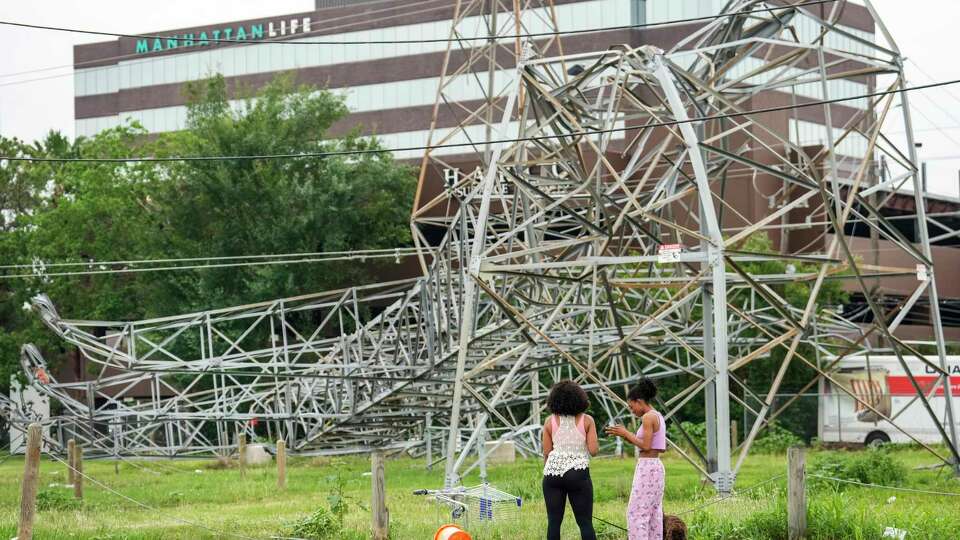 Emilia Kobina, left, and Denise Kobina take a look at a fallen transmission line tower along the US 290 feeder road in the aftermath of a severe storm on Friday, May 17, 2024 in Houston. Fast-moving thunderstorms pummeled southeastern Texas for the second time this month, killing at least four people, blowing out windows in high-rise buildings, downing trees and knocking out power to more than 900,000 homes and businesses in the Houston area.