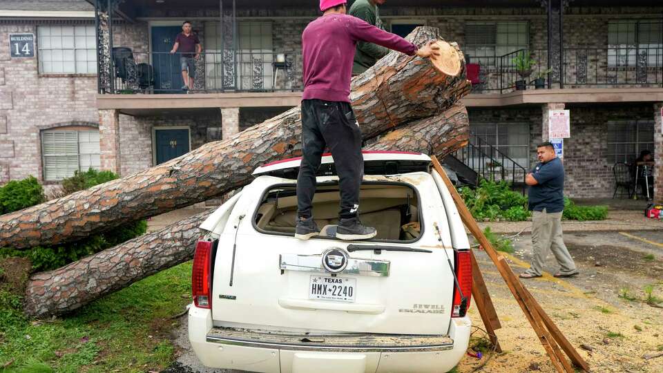 Tree service crews climb atop an SUV to cut apart a tree that fell on it at an apartment complex in the 4600 block of Sherwood in the aftermath of a severe storm on Friday, May 17, 2024 in Houston. Fast-moving thunderstorms pummeled southeastern Texas for the second time this month, killing at least four people, blowing out windows in high-rise buildings, downing trees and knocking out power to more than 900,000 homes and businesses in the Houston area.