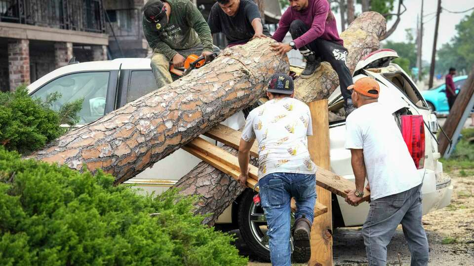 Tree service crews climb atop an SUV to cut apart a tree that fell on it at an apartment complex in the 4600 block of Sherwood in the aftermath of a severe storm on Friday, May 17, 2024 in Houston. Fast-moving thunderstorms pummeled southeastern Texas for the second time this month, killing at least four people, blowing out windows in high-rise buildings, downing trees and knocking out power to more than 900,000 homes and businesses in the Houston area.