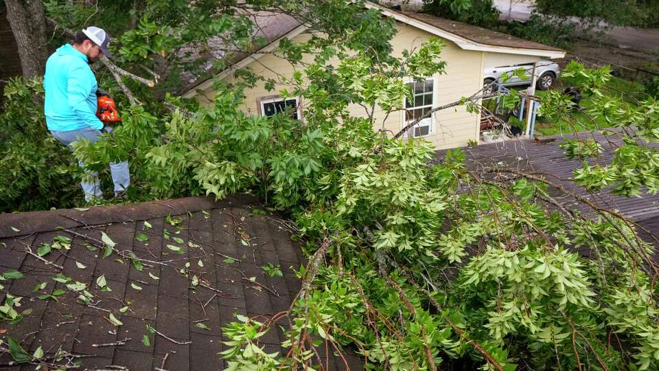 Isiah Turner, a volunteer with Trae the Truth's Relief Gang, cuts branches from a tree that fell onto the roof of Carrie Turner's home in the 200 block of De Haven, in the aftermath of a severe storm on Friday, May 17, 2024 in Houston. Fast-moving thunderstorms pummeled southeastern Texas for the second time this month, killing at least five people, blowing out windows in high-rise buildings, downing trees and knocking out power to more than 900,000 homes and businesses in the Houston area.