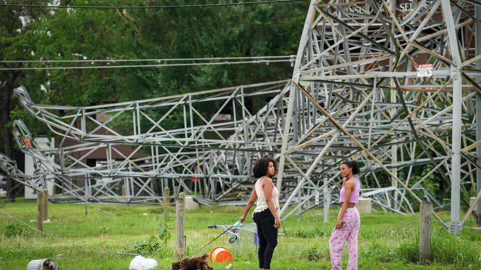 Emilia Kobina, left, and Denise Kobina stand near a fallen transmission line tower along the US 290 feeder road in the aftermath of a severe storm on Friday, May 17, 2024 in Houston. CenterPoint Energy has incurred at least $100 million in costs restoring power following the storm, according to a company executive.