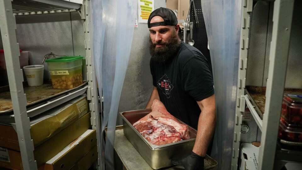 Zach Cook loads meet into a cooler in the aftermath of destructive storms Thursday, May 23, 2024, at Feges BBQ in Houston. The restaurant's owner Patrick Feges said they had just had power restored the day before, and that food was delivered that morning.