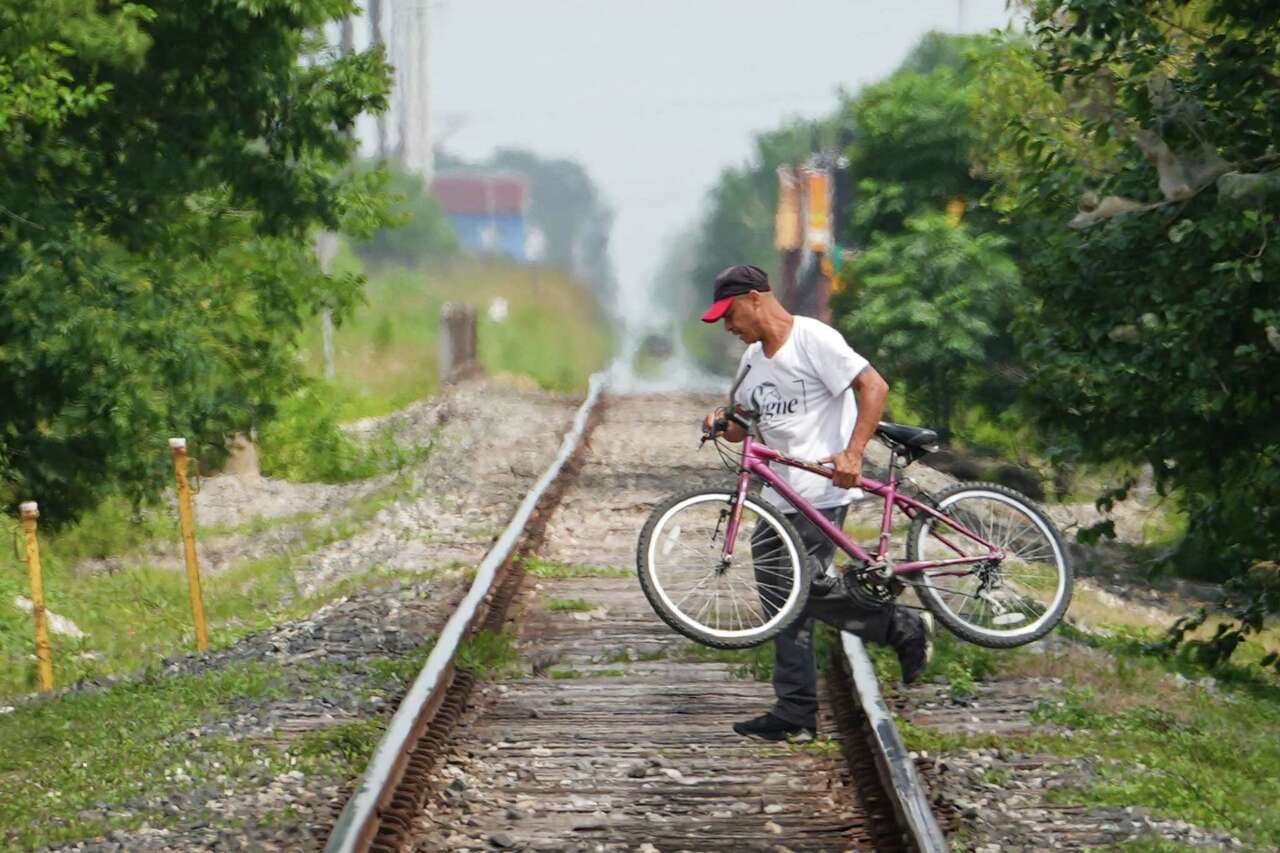 A man carries a bicycle across railroad tracks as he commutes in the mid-afternoon heat Friday, May 24, 2024, near Cesar Chavez High School in Houston.