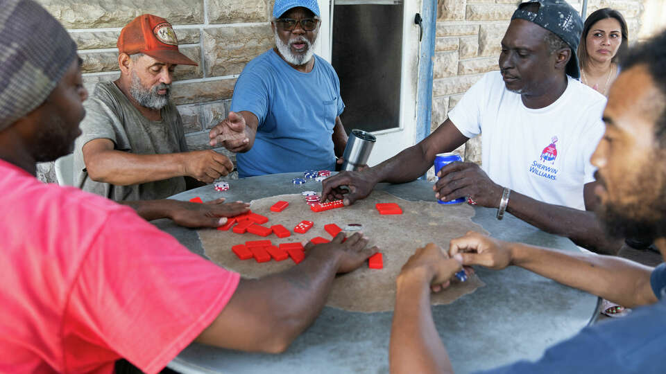 Neighbors take refuge from the 100-degree weather under the shade of Robert Paterson's front porch for a game of dominos in Kashmere Gardens, Saturday, May 25, 2024, in Houston.