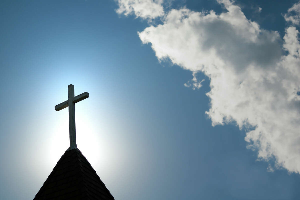 A wood cross on an old church steeple backlighted by a rising sun. (Stock photo)