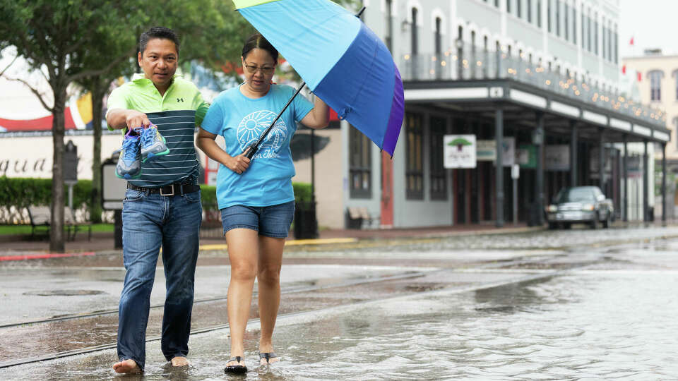 Roy Quiroz and his wife, Minda, cross a flooded section of The Strand near Kempner Street as rain from Potential Tropical Cyclone One continues, Wednesday, June 19, 2024, in Galveston.