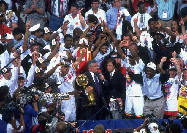 Houston Rockets Hakeem Olajuwon (34), Kenny Smith (30), and teammates victorious with NBA commissioner David Stern, NBC Sports announcer Bob Costas, and Larry O'Brien Championship Trophy after winning Game 7 and championship series vs New York Knicks at The Summit. 