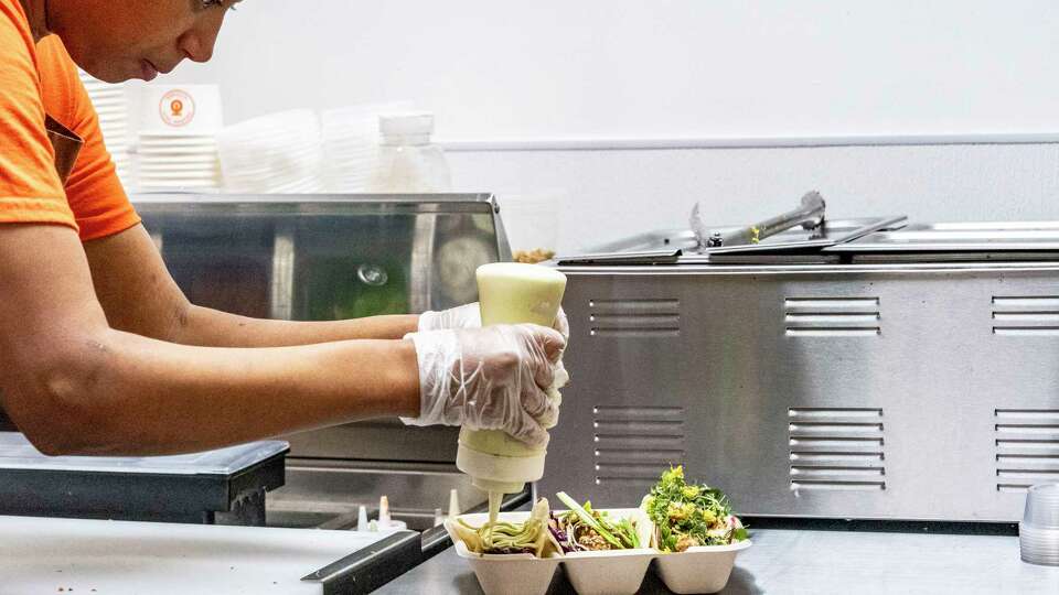 Co-owner Houston Adegoke dribbles on sauce as she prepares an orange taco Tuesday, June 25, 2024 at Orange Taco downtown, in the Highlight at Houston Center.