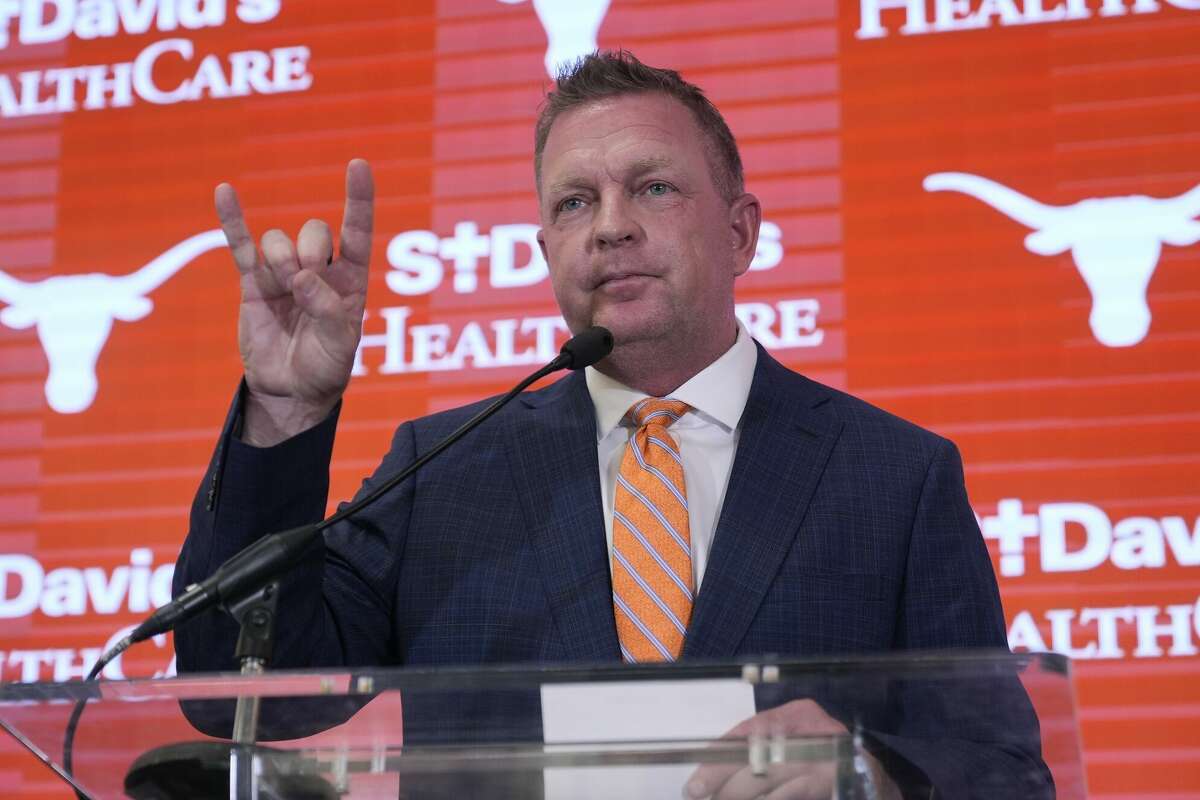 Jim Schlossnagle flashes a hook'em sign as he speaks at a news conference after he was introduced as the new NCAA college head baseball coach at Texas, Wednesday, June 26, 2024, in Austin, Texas. Schlossnagle left rival program Texas A&M. (AP Photo/Eric Gay)