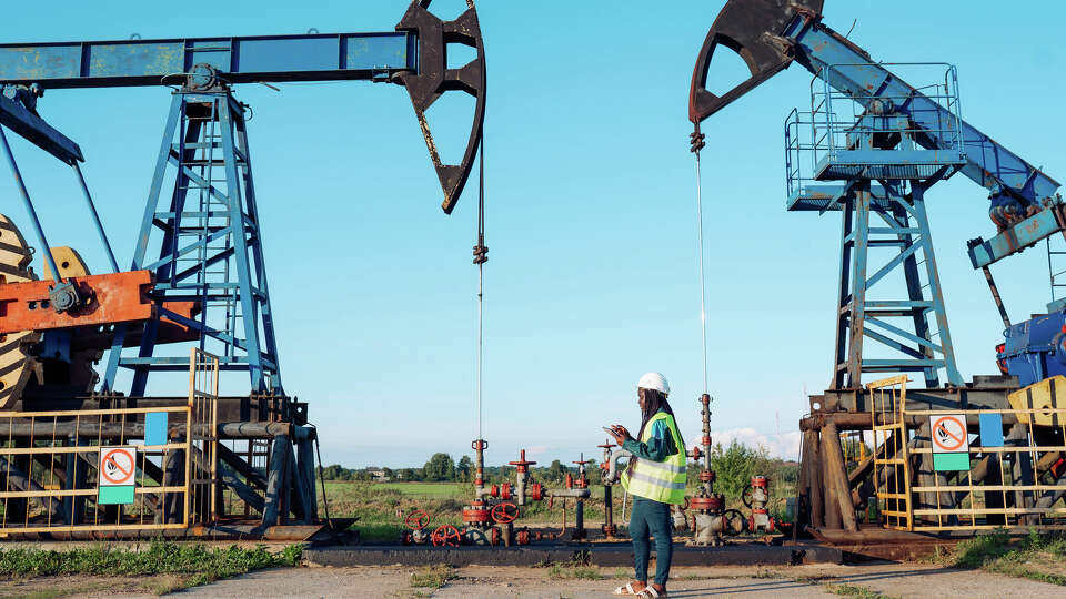 Female engineer oversees oil rig operations: African American woman with digital tablet in hand, conducts safety checks on oil pump jacks