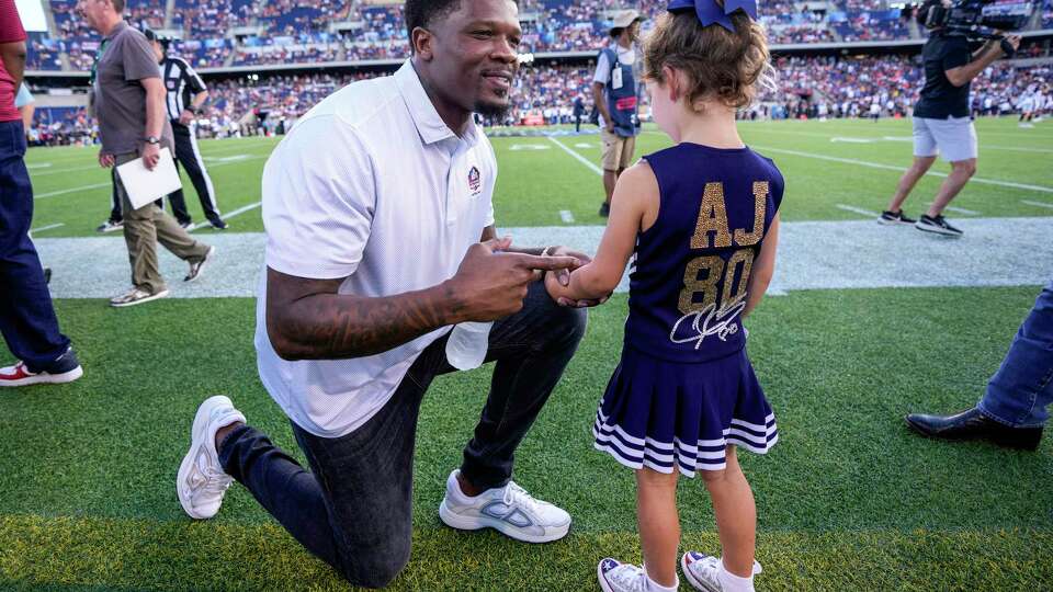 Former Houston Texans wide receiver Andre Johnson, a member of the Pro Football Hall of Fame Class of 2024, kneels down to talk to Hunter McNair, daughter of Cal and Hannah McNair, before the Hall of Fame Game on Thursday, Aug. 1, 2024 in Canton, Ohio.