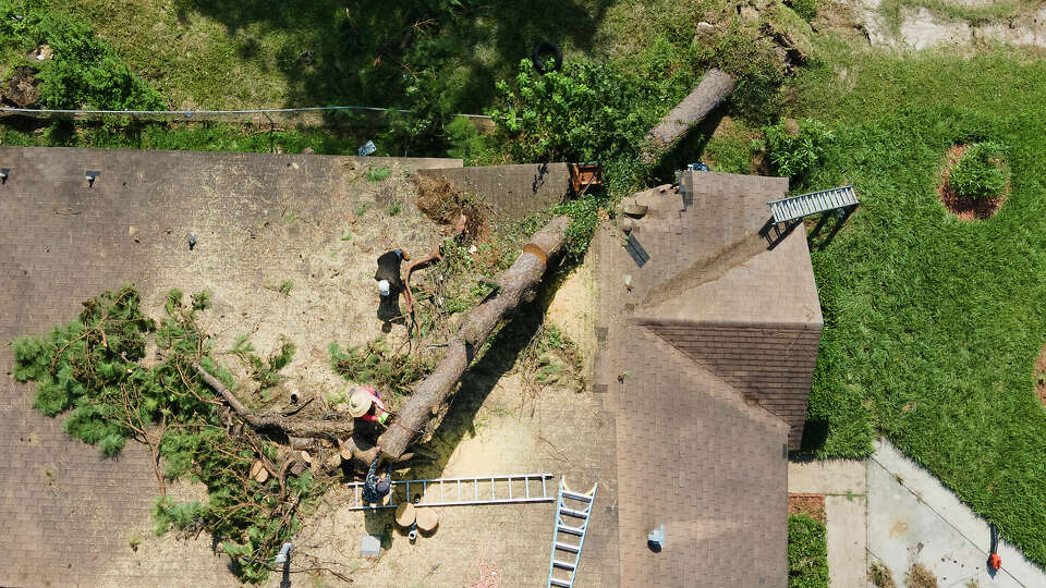 Employees of Premier Home Improvement remove a tree off of the roof of a home in the Homestead neighborhood of Houston on Wednesday, July 10, 2024.