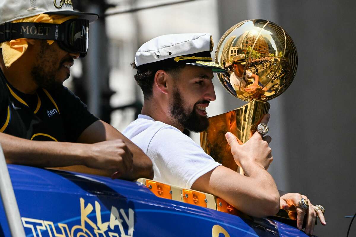 Otto Porter Jr. (L) and Klay Thompson hold a trophy as they wave from a double decker bus while basketball fans cheer during the Golden State Warriors NBA Championship victory parade along Market Street on June 20, 2022 in San Francisco, California. - Tens of thousands of fans poured onto the streets of San Francisco on Monday to salute the victorious Golden State Warriors as the team celebrated its fourth NBA championship in eight seasons with an open-top bus parade.