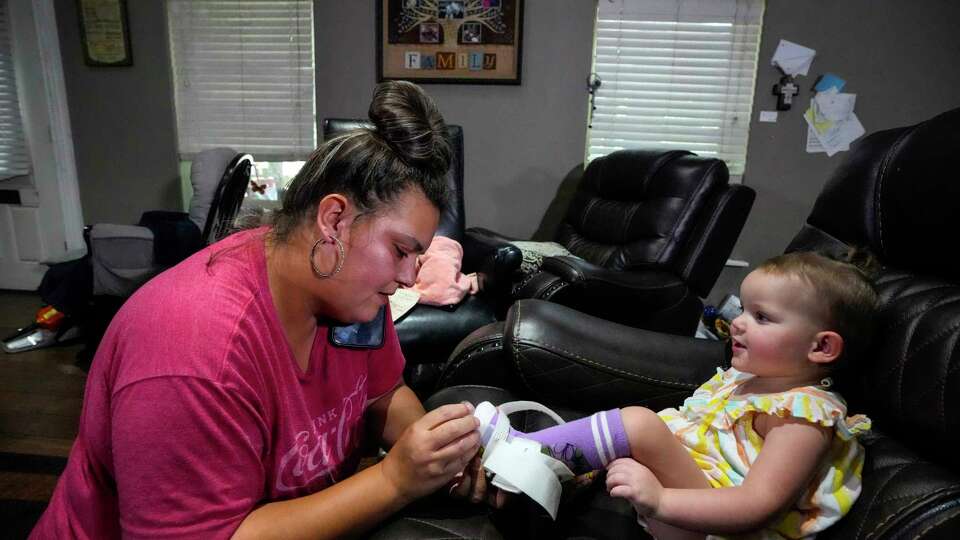 Jessica Navarro fits ankle-foot orthosis (AFO) braces on her daughter, Kaelyn Duffey’s, ankles on Monday, Aug. 12, 2024 in Porter. Kaelyn, 1, was diagnosed with cerebral palsy after suffering a stroke at birth. She attended regular outpatient therapy appointments at Texas Children's Hospital to regain some brain function, but her parents recently learned that all of her therapists had been laid off.