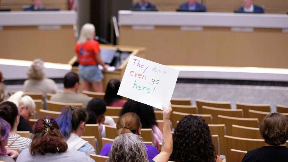 An attendee holds up a sign pointing out that the speaker Megan Jasper, in red, is not a resident of the district as Jasper speaks in favor of the board during the regular meeting of Cy-Fair ISD school board meeting Monday, Aug. 12, 2024 in Cypress, TX.