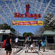 Two visitors jokingly dance as they walk underneath a "Welcome Back" sign at Six Flags Magic Mountain on its first day of reopening to members and pass holders in Valencia, Calif., Thursday, April 1, 2021.