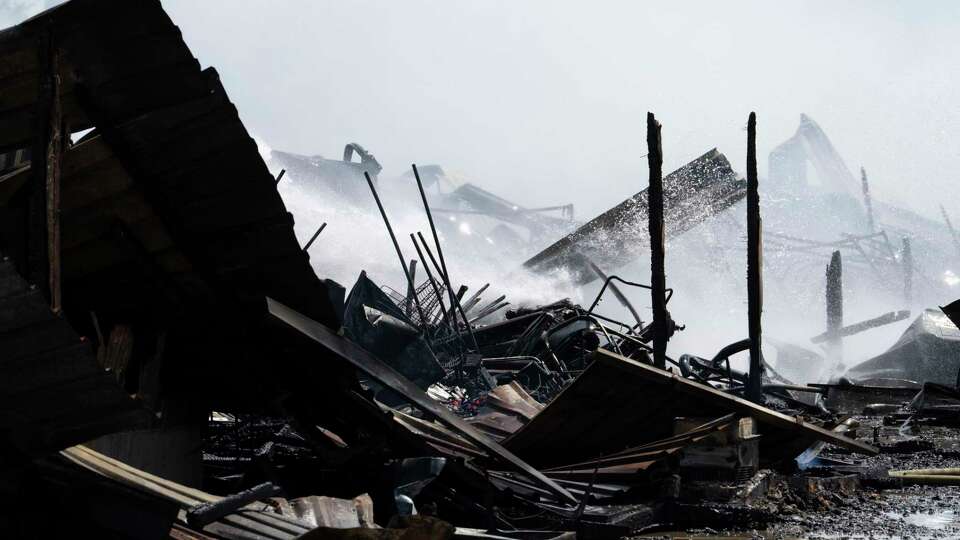 Smoke and steam rise as water is sprayed on the smoldering remains of vender booths after a fire broke out at a flea market on Airline Drive Friday, Aug. 16, 2024.