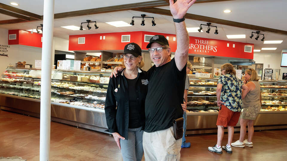 Husband and wife owners Bobby and Janice Jucker wave at a customer as they stand inside Three Brothers Bakery on South Braeswood in Houston, TX on August 9, 2024. The Jewish bakery has survived four floods, including Hurricane Harvey.