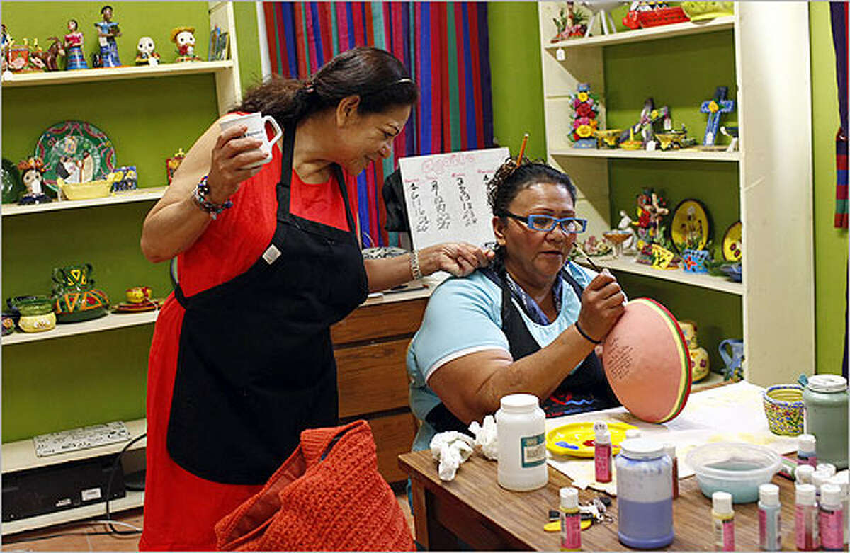 Coordinator Imelda Arizmendez (left) looks at the earrings worn by Grace Gonzalez while Gonzalez paints the rim of a bowl at MujerArtes, the Esperanza Center's women's clay co-op.
