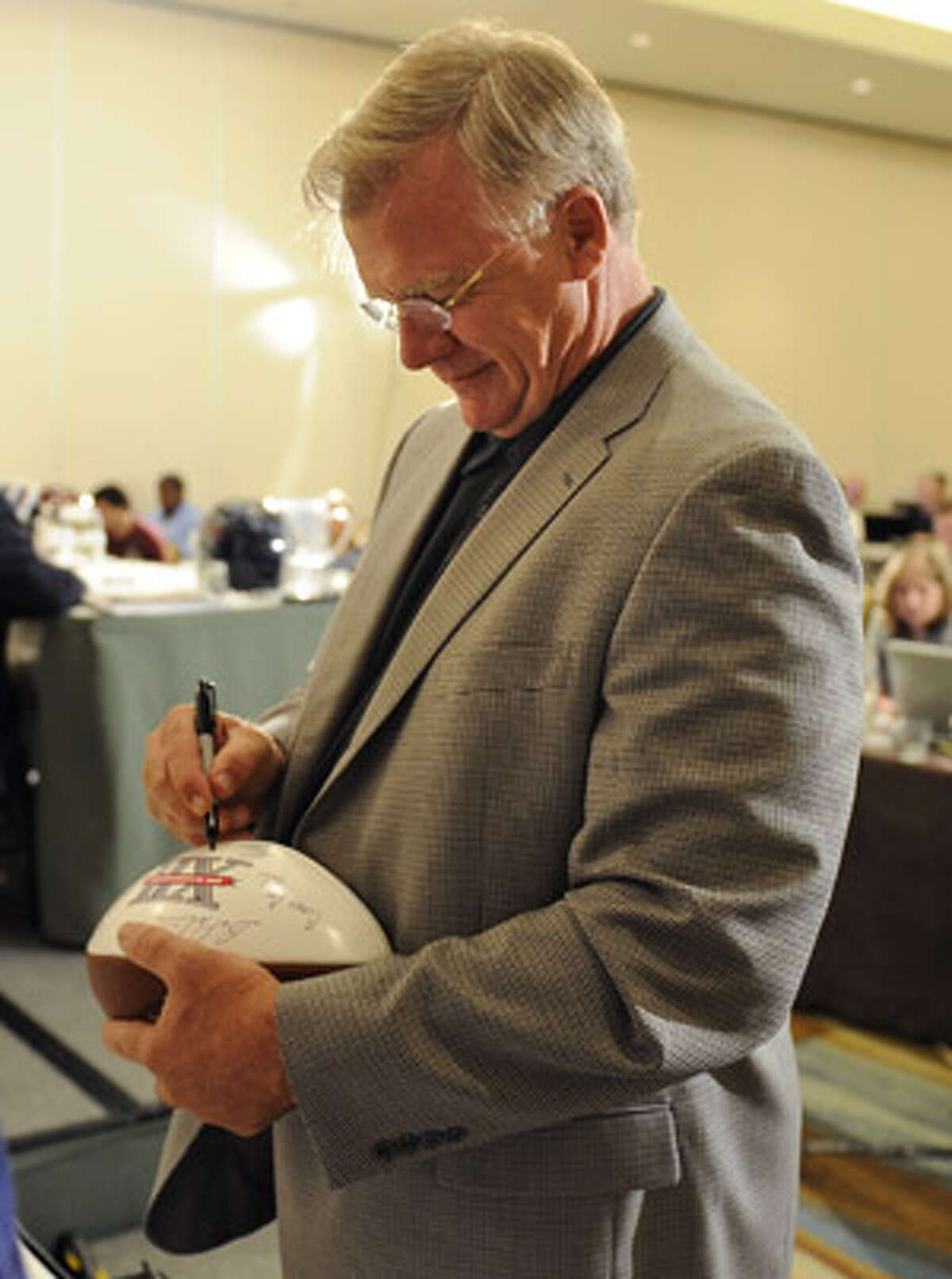 A&M coach Mike Sherman autographs a football before a news conference at Big 12 Football Media Day.