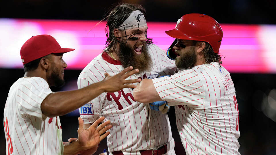 Philadelphia Phillies' Bryce Harper, right, celebrates with Brandon Marsh, center, and Johan Rojas after hitting a game-winning RBI-single against Houston Astros pitcher Josh Hader during the 10th inning of a baseball game, Monday, Aug. 26, 2024, in Philadelphia. (AP Photo/Matt Slocum)