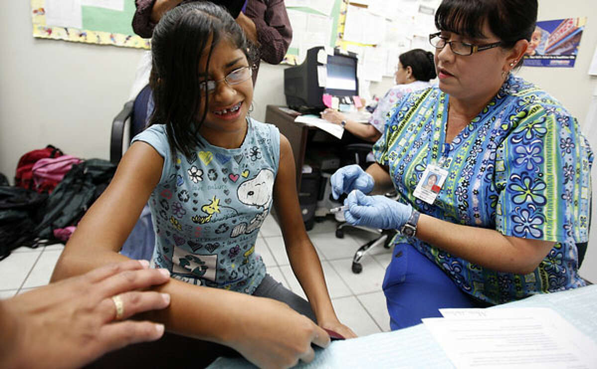 Nurse Rosamaria Vasquez, right, vaccinates Isabelle Salinas, 12, at the city-run immunization clinic inside the Goodwill Store on Blanco Road and Loop 410.