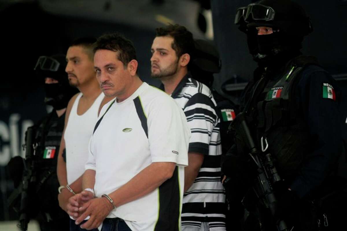 Jesus Ernesto Chavez, known as "El Camello" (second from left) stands as he is guarded by federal police during a presentation to the press, in Mexico City, Friday, July 2, 2010. According to the federal police Chavez ordered the March 13 attack that killed a U.S. consulate employee and her husband as they drove in the violent border city. The other two detained men are unidentified.