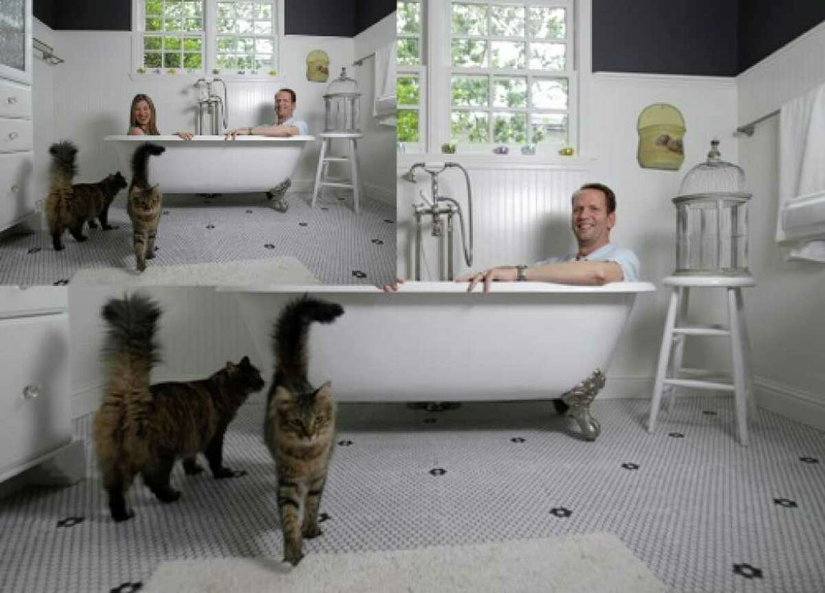 Cats Ron and Nancy walk by Dwayne and Sarah Van Wieren as the two sit in a claw-foot tub in their new home, which they qualified for with 100 percent financing and no money down.