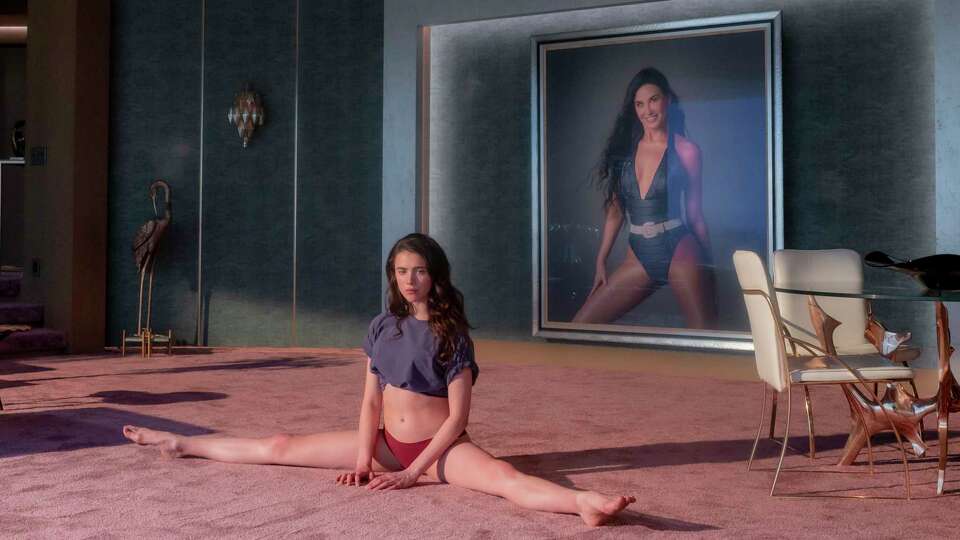 Margaret Qualley in front of a portrait of Demi Moore in 'The Substance.'