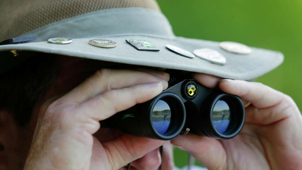 Brian Sinclair, with National Park pins on the brim of his hat, uses binoculars to spot birds during The Great Texas Birding Classic, an annual bird watching tournament held across Texas at Lakeside Park Saturday, May 14, 2022 in The Woodlands, TX.