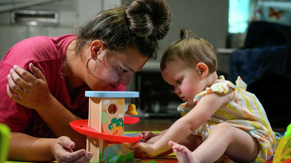 Jessica Navarro plays with her daughter, Kaelyn Duffey, on her play mat on Monday, Aug. 12, 2024 in Porter. Kaelyn, 1, was diagnosed with cerebral palsy after suffering a stroke at birth. Kaelyn's therapists at Texas Children's Hospital were laid off in mid-August, but she has new therapists now after a round of rehirings this month.